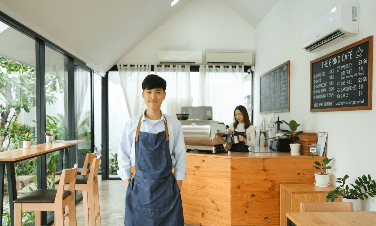 Greater Boston small business owner standing inside a bright cafe — the kind of SMB that benefits from Mass Save commercial heat pump rebates in 2026